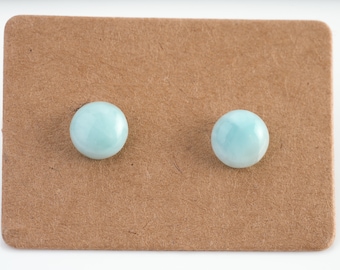 May include: A pair of light blue gemstone stud earrings on a brown card.