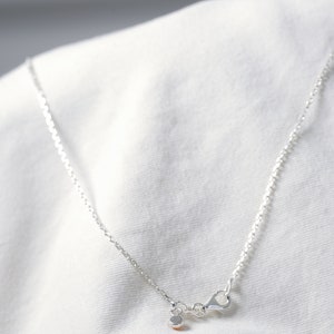 May include: A silver chain necklace with a small silver clasp. The necklace is on a white fabric background.