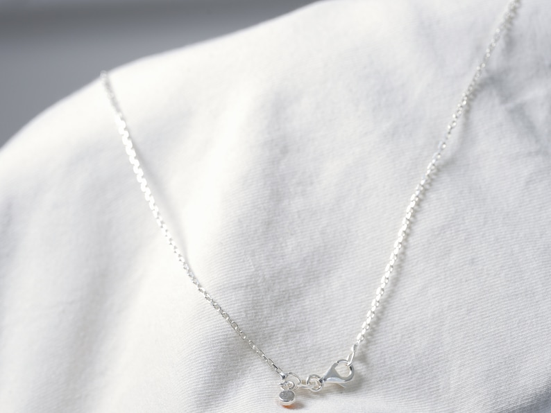May include: A silver chain necklace with a small silver clasp. The necklace is on a white fabric background.