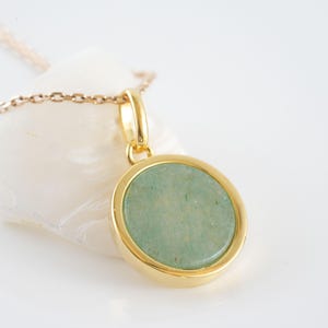 Puede incluir: Un collar de oro con un colgante redondo que presenta una piedra verde claro.