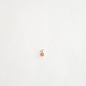 May include: A small, round, orange gemstone pendant with a silver bail.