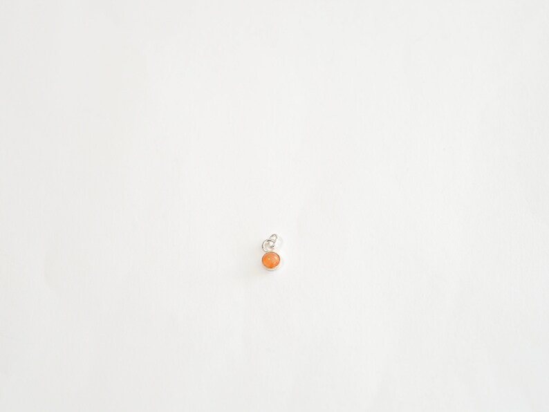 May include: A small, round, orange gemstone pendant with a silver bail.