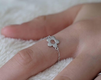 May include: A silver ring with a delicate chain and a flower-shaped design. The flower has a hollow center.