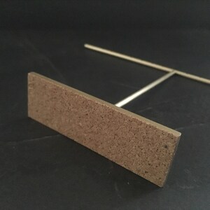 Pode incluir: Um suporte de metal dourado com uma base retangular de corti&ccedil;a. O suporte &eacute; projetado para segurar joias ou outros itens pequenos.