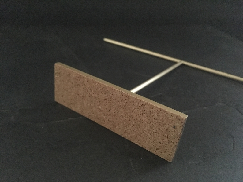 Pode incluir: Um suporte de metal dourado com uma base retangular de corti&ccedil;a. O suporte &eacute; projetado para segurar joias ou outros itens pequenos.
