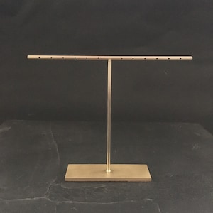 Peut inclure: Un pr&eacute;sentoir &agrave; bijoux en m&eacute;tal dor&eacute; avec une longue barre horizontale et plusieurs trous pour tenir les boucles d'oreilles. Le pr&eacute;sentoir a une base rectangulaire.