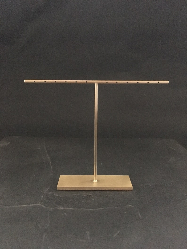 Peut inclure: Un pr&eacute;sentoir &agrave; bijoux en m&eacute;tal dor&eacute; avec une longue barre horizontale et plusieurs trous pour tenir les boucles d'oreilles. Le pr&eacute;sentoir a une base rectangulaire.