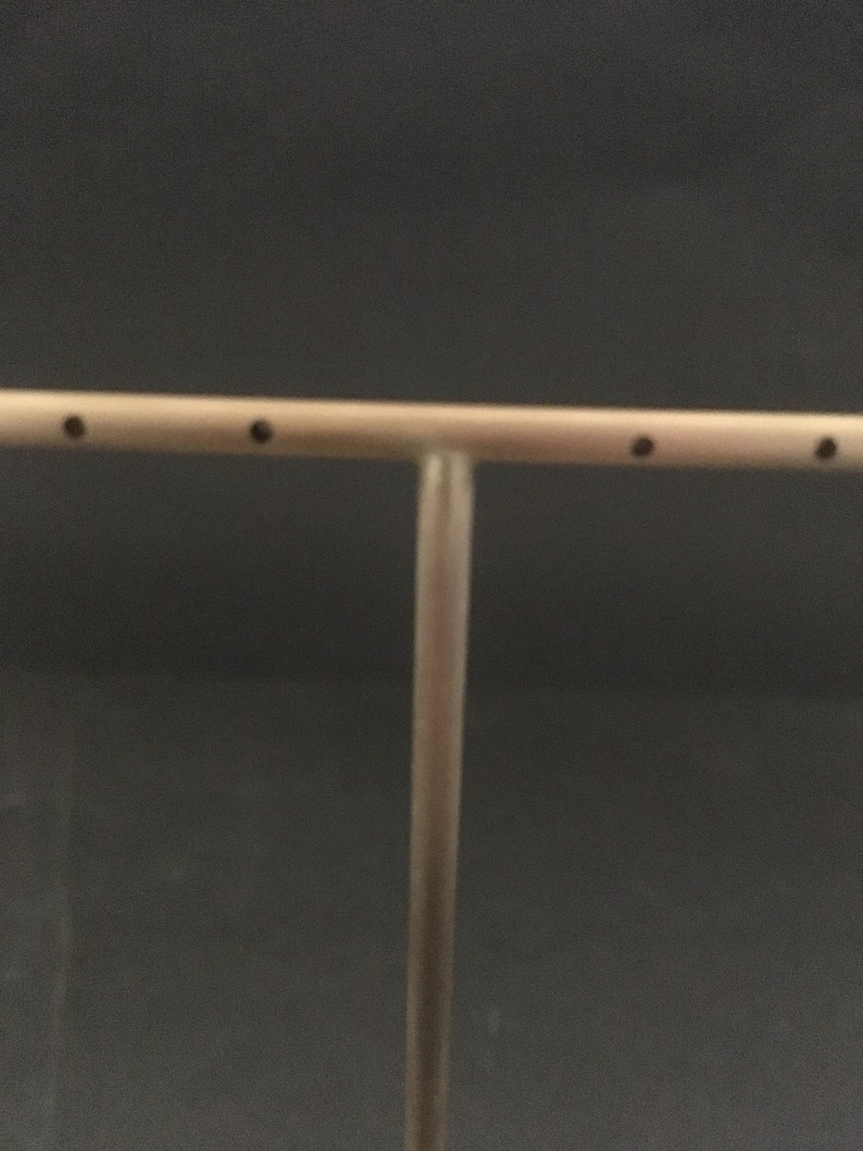 Peut inclure: Un pr&eacute;sentoir &agrave; bijoux en m&eacute;tal argent&eacute; avec une barre horizontale et un poteau vertical. La barre comporte quatre petits trous pour tenir les boucles d'oreilles.