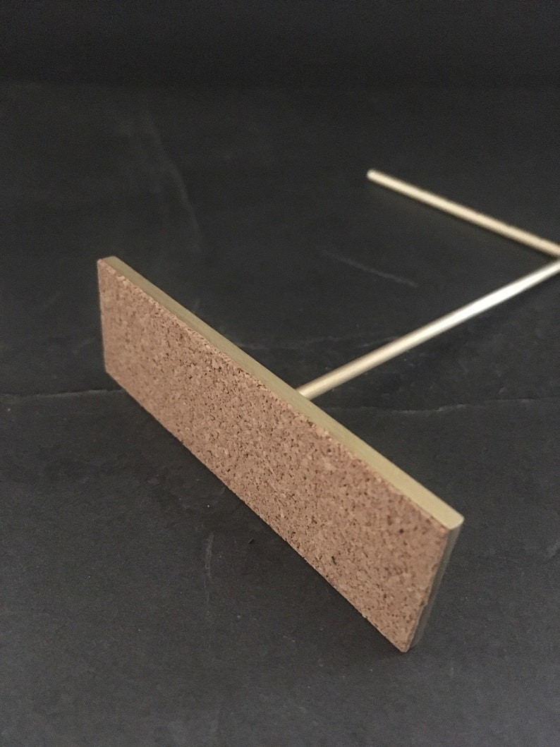 Peut inclure: Un support en m&eacute;tal dor&eacute; avec une base rectangulaire en li&egrave;ge. Le support est con&ccedil;u pour tenir un petit objet, comme un t&eacute;l&eacute;phone ou un livre.