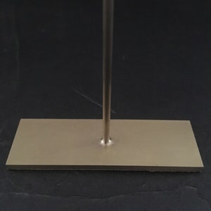 Peut inclure: Un support en m&eacute;tal argent&eacute; avec une base rectangulaire. Le support a une seule tige verticale qui s'&eacute;tend de la base.