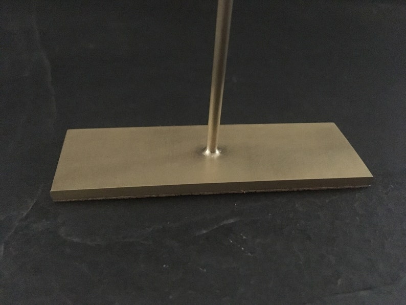 Pode incluir: Um suporte de metal dourado com uma base retangular e uma &uacute;nica haste vertical.