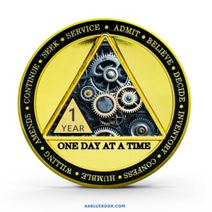 May include: A round gold and black medallion featuring a central triangle filled with metallic gears. The triangle displays the text 1 YEAR. The outer border contains the words SEEK, SERVICE, ADMIT, BELIEVE, DECIDE, INVENTORY, CONFESS, HUMBLE, WILLING, AMENDS, CONTINUE. The text ONE DAY AT A TIME is printed below the triangle.