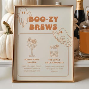 Könnte beinhalten: Eine Halloween-Getränkeausstellung mit weißen Kürbissen, Flaschen und einem Schild mit der Aufschrift "BOO-ZY BREWS". Das Schild listet Cocktailrezepte auf: Poison Apple Sangria und The Devil's Spicy Margarita. Der weiße Wagen hat goldene Details.
