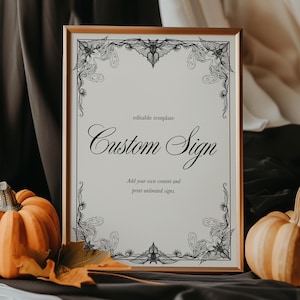 May include: A framed sign with the text "Custom Sign" in elegant script, surrounded by decorative black floral elements. The sign is displayed with pumpkins, a candle, and autumn leaves, creating a fall or Halloween theme.