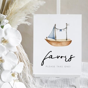May include: A white sign with a watercolor illustration of a sailboat with a blue sail and a string of flags. The sign says "favors" in black cursive writing and "Please take one!" in smaller black text.