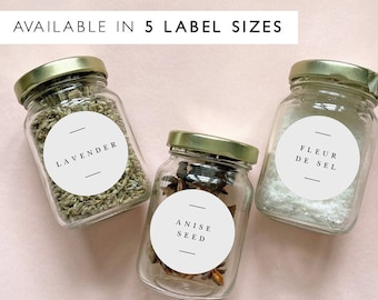 Puede incluir: Tres frascos de vidrio con tapas doradas y etiquetas redondas blancas. Las etiquetas tienen texto negro que dice "Lavender", "Anise Seed" y "Fleur de Sel".