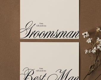 Peut inclure: Deux cartes rectangulaires blanc cassé avec du texte noir. La carte du haut indique "Liam, will you be my Groomsman" dans un mélange de polices serif et script. La carte du bas indique "Liam, will you be my Best Man" avec les mêmes polices.