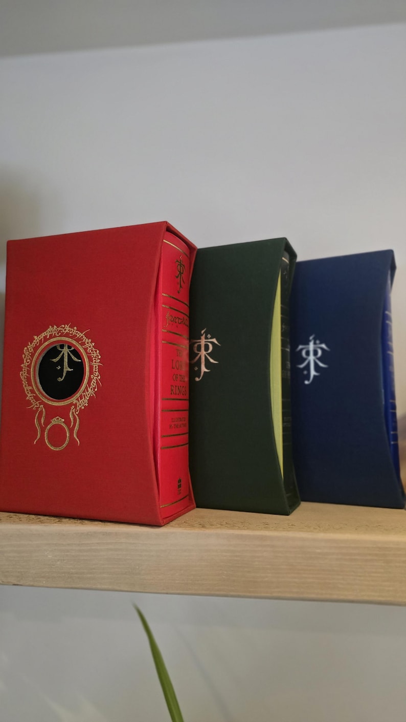 Pode incluir: Tr&ecirc;s livros de capa dura com capas vermelha, verde e azul. Os livros s&atilde;o todos do mesmo tamanho e t&ecirc;m um design semelhante. As capas apresentam um s&iacute;mbolo estilizado e o t&iacute;tulo "O Senhor dos An&eacute;is" no livro vermelho.