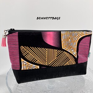 May include: A black zippered pouch with a pink, yellow and white geometric pattern. The pouch has a black tassel zipper pull.