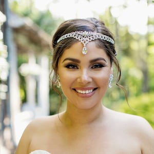 Peut inclure: Une mariée portant une robe de mariée blanche sans bretelles avec un bandeau perlé et un bouquet de roses blanches.