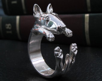 Puede incluir: Un anillo de plata con una escultura detallada de un bull terrier. El perro está representado en una pose juguetona, con las patas levantadas y la cabeza inclinada. El anillo es una pieza de joyería única y llamativa.