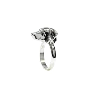 May include: A silver ring featuring a detailed dog head design. The ring is made from sterling silver and has a polished finish.