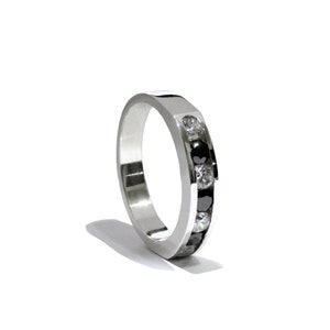 May include: A silver band ring with a row of black and white diamonds set into the band.