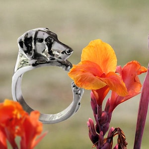 May include: A silver ring featuring a detailed sculpture of a dog's head, with the dog's nose touching a bright orange flower.