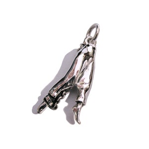 Puede incluir: Un amuleto de plata con forma de piernas, con los pies apuntando hacia arriba. El amuleto está diseñado para ser usado en un collar o pulsera.