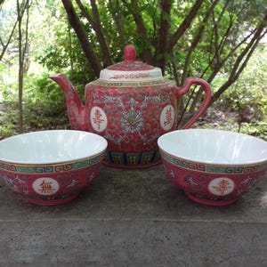 May include: A red and white ceramic tea set with a teapot and two bowls. The teapot has a lid and handle, and the bowls are round. The set is decorated with floral patterns and Chinese characters.