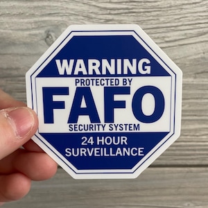 May include: An octagonal warning sign with a blue background and white text. The sign reads "WARNING PROTECTED BY FAFO SECURITY SYSTEM 24 HOUR SURVEILLANCE".