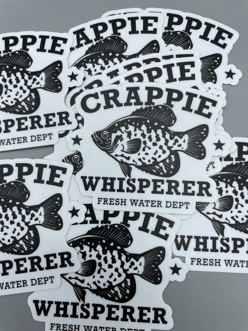 Op de afbeelding: Een stapel zwart-wit stickers met een visafbeelding en de tekst "Crappie Whisperer Fresh Water Dept" en "Appie Whisperer Fresh Water Dept".