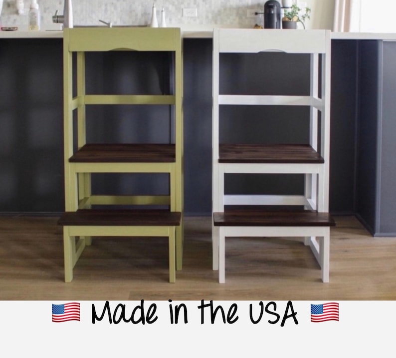 Puede incluir: Dos taburetes de escalera de madera, uno en verde y otro en blanco, con pelda&ntilde;os de madera marr&oacute;n oscuro. Ambos taburetes tienen un estante superior y un pelda&ntilde;o inferior. El texto "Made in the USA" est&aacute; impreso debajo de los taburetes.