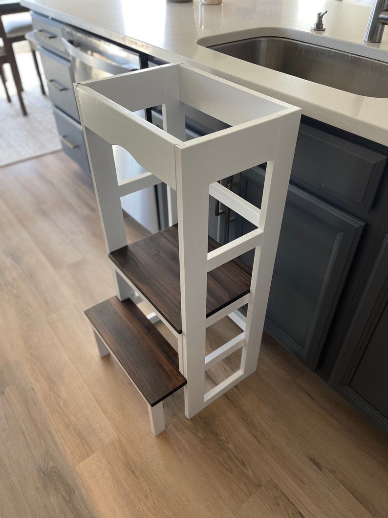 Puede incluir: Taburete de madera blanco con tres pelda&ntilde;os y una parte superior de madera marr&oacute;n. El taburete est&aacute; en una cocina junto a un fregadero.