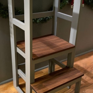 Puede incluir: Un taburete de madera gris con dos pelda&ntilde;os y una plataforma superior. Los pelda&ntilde;os y la plataforma son de madera oscura. El taburete est&aacute; sobre un suelo de madera.