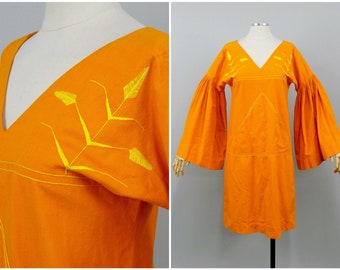 May include: Orange vintage dress with yellow embroidery. The dress has a V-neckline, long sleeves, and a loose fit.