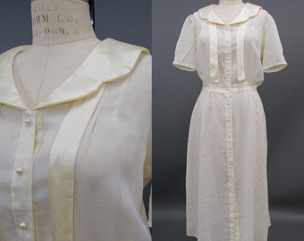 Puede incluir: Un vestido blanco de gasa con cuello marinero y cierre de botones en la parte delantera. El vestido tiene un corpiño ajustado y una falda fluida. El vestido está hecho de una tela ligera y tiene un tacto delicado.