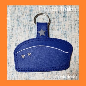 May include: Blue leather keychain with a white star and two white stars on the front. The keychain has a silver metal ring.