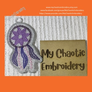 May include: Purple and white embroidered dreamcatcher with pink and purple feathers. The dreamcatcher is on a white background with a brown card that says "My Chaotic Embroidery".