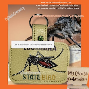 Op de afbeelding: Een beige leren sleutelhanger met een groene strasssteen en een geborduurd beeld van een mug. De tekst "STATE BIRD" is geborduurd onder de mug. De tekst "Use a micro font to add your state name" is gedrukt boven de mug. De sleutelhanger is bevestigd aan een metalen ring.