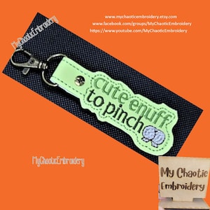 May include: A green and white embroidered keychain with the text "cute enuff to pinch".