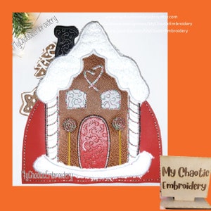 May include: A gingerbread house with white icing and candy cane accents. The house is decorated with a red door and candy cane windows. The house is sitting on a red background with the text "My Chaotic Embroidery" on the bottom left corner.