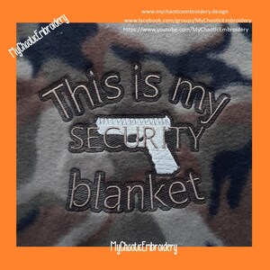 May include: A brown and tan camouflage fabric blanket with the text "This is my security blanket" embroidered in brown thread. A white outline of a handgun is embroidered above the word "security".