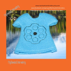 May include: A light blue felt t-shirt with a black embroidered design of a gun barrel with six chambers. The t-shirt is on a blue and white background.