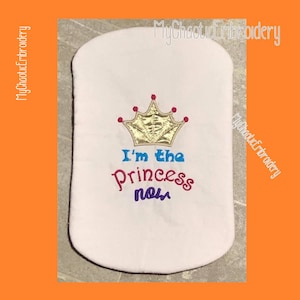 May include: White fabric with embroidered text "I'm the Princess now" and a gold crown with red jewels.