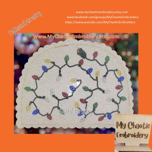May include: A white, glittery, semi-circular embroidery design of a string of Christmas lights with multi-colored bulbs. The design is surrounded by a gold scalloped edge. The design is on a white background. The text "My Chaotic Embroidery" is on a wooden sign in the lower right corner of the image.