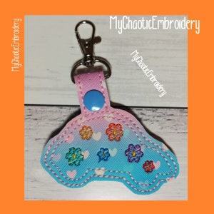 May include: A blue and pink car-shaped keychain with embroidered flowers and hearts. The keychain has a silver metal ring and a blue button.