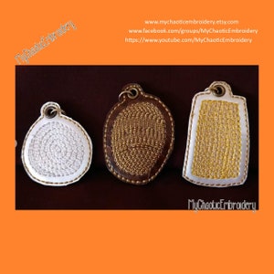 May include: Three embroidered keychains with different designs. The keychains are white with gold and brown stitching. The keychains are on a brown surface.  MyChaoticEmbroidery