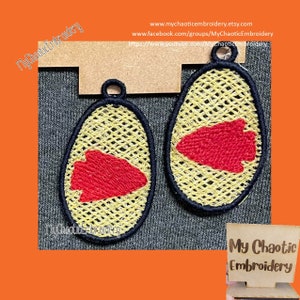 Può includere: Due toppe ricamate con un design a freccia rossa su sfondo giallo. Le toppe sono di forma ovale e hanno un contorno nero. Le toppe sono appese a un espositore in legno. L'espositore ha il testo "My Chaotic Embroidery".
