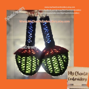 May include: Two crocheted ornaments shaped like cherries with green, red, and blue details. The ornaments are hanging from a white string. The text "My Chaotic Embroidery" is visible in the image.